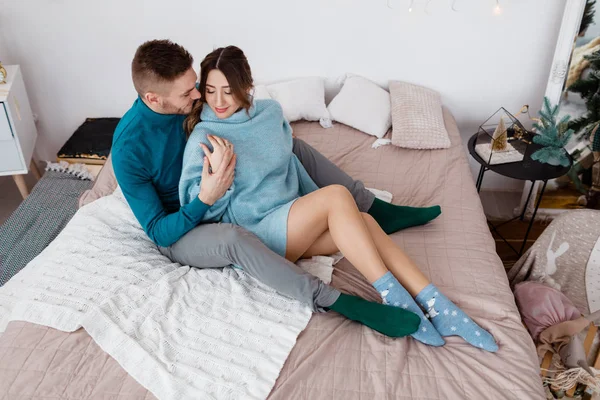 Famiglia, Natale, vacanze, amore e concetto di persone - felice coppia elegante in maglioni blu seduti sul letto a casa — Foto Stock