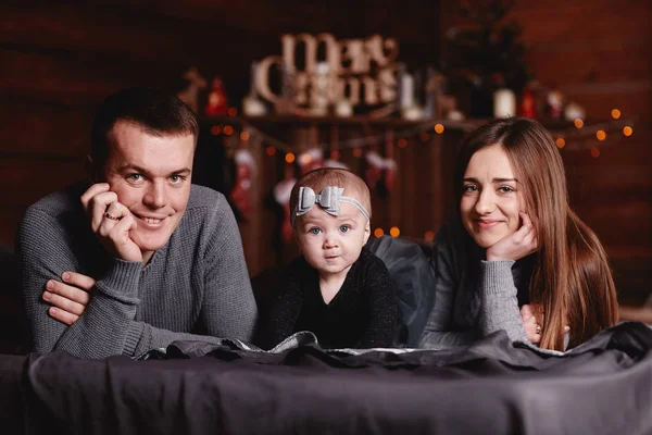 Bonito jovem família com pai, mãe e bebê menina na cama com fundo de Natal atrás. — Fotografia de Stock