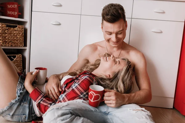 Linda menina sentada no chão e se divertindo com o namorado. Jovem casal desfrutando de café ou chá na cozinha. feliz dia dos namorados . — Fotografia de Stock