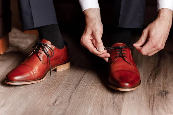 Novio ató los cordones en los zapatos de cerca. hombre de negocios está colgando zapatos interiores en la habitación de hotel. mans manos y par de zapatos de hombre de cuero. reunión del novio. mañana del hombre de negocios . — Foto de Stock