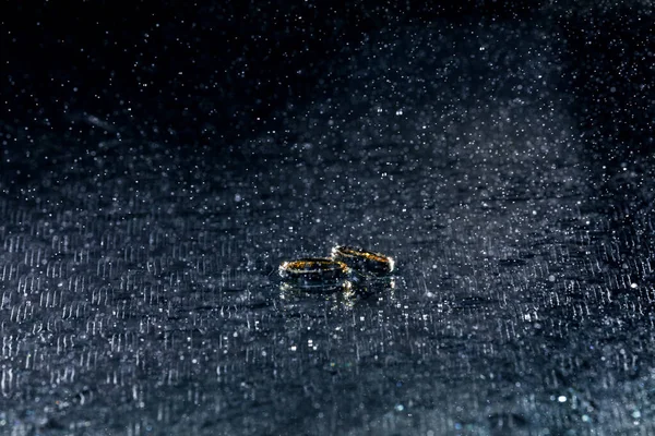 Anéis de ouro do casamento em gotas de água no fundo azul — Fotografia de Stock