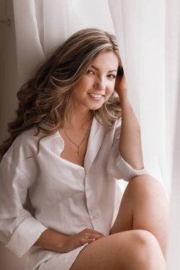 Young female blonde model in window light. Woman near Window. Dream and Relax, tender girl in the Morning in the Bedroom window