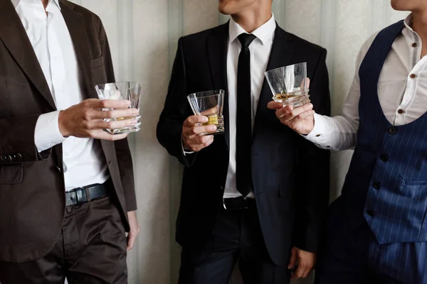 Стильные друзья бизнесмены в костюмах тост со стаканами виски в помещении, крупным планом. утро женихов — стоковое фото