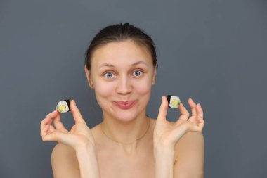 Closeup portrait of beautiful young funny woman eating and playing with sushi rolls on a grey background. Copy space