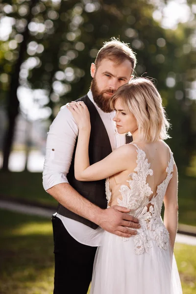 Elegante joven hermosa pareja abrazándose en el parque de primavera en un día soleado. retrato de boda. Mujer en vestido blanco . —  Fotos de Stock