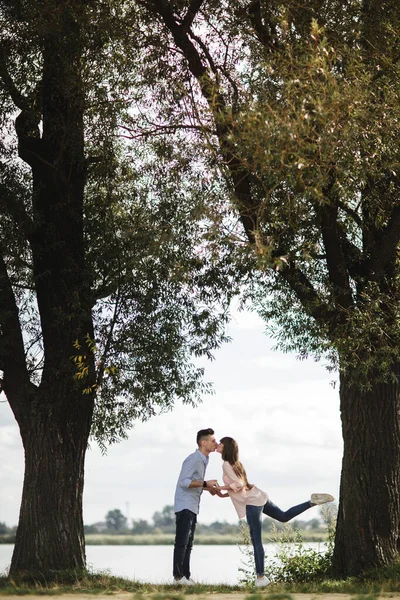 Junges romantisches Paar vergnügt sich an einem sonnigen Sommertag in der Nähe des Sees. Wir genießen die gemeinsame Zeit im Urlaub. Mann und Frau umarmen und küssen sich. — Stockfoto