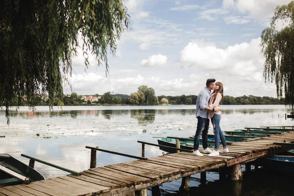 Genç romantik çift yazın göl kenarında güneşli bir günde eğleniyor. Tatilde birlikte vakit geçirmenin tadını çıkarıyorum. Erkek ve kadın sarılıp öpüşüyor.. — Stok fotoğraf