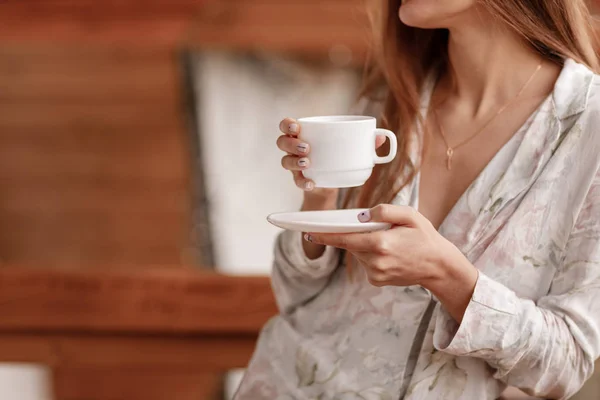 Junge Frau auf dem Balkon mit einer Tasse Kaffee oder Tee am Morgen. sie im Hotelzimmer mit Blick auf die Natur im Sommer. Mädchen trägt stylische Nachtwäsche. Entspannungszeit — Stockfoto