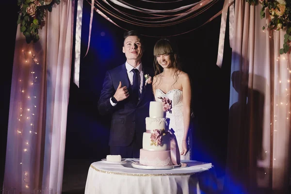 A menyasszony és a vőlegény kint állnak egy nagy esküvői torta mellett. esküvő napja — Stock Fotó