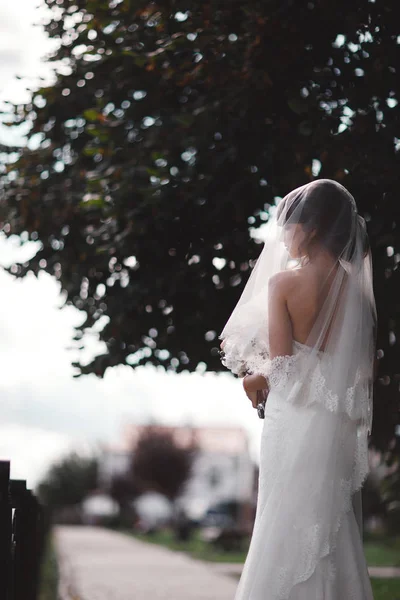 Beyaz lüks elbiseli, duvak takmış ve bir buket çiçekle dışarıda poz veren güzel bir gelin. Düğün portresi. Boşluğu kopyala — Stok fotoğraf