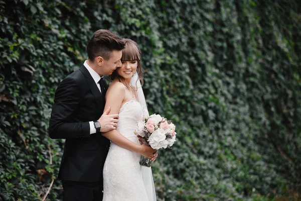 Noiva e noivo no dia do casamento andando ao ar livre na primavera natureza verde. Casal nupcial, mulher recém-casada feliz e homem abraçando no parque verde. Casal de amor ao ar livre. Noiva e noivo — Fotografia de Stock