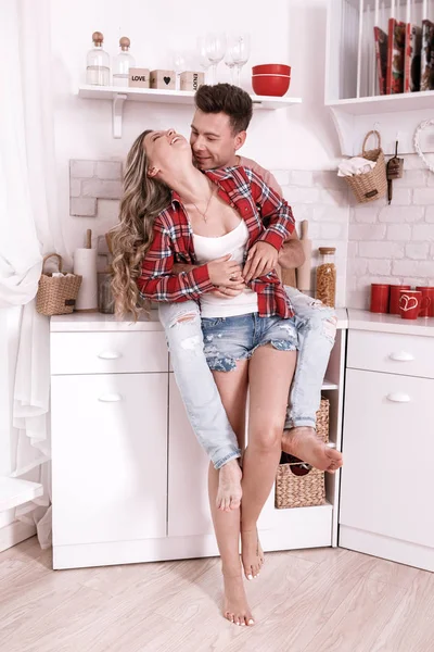 Szczęśliwa młoda zakochana para przytula się i bawi w kuchni w Walentynki rano. Stylowy mężczyzna i kobieta z długimi włosami relaksują się w domu. — Zdjęcie stockowe
