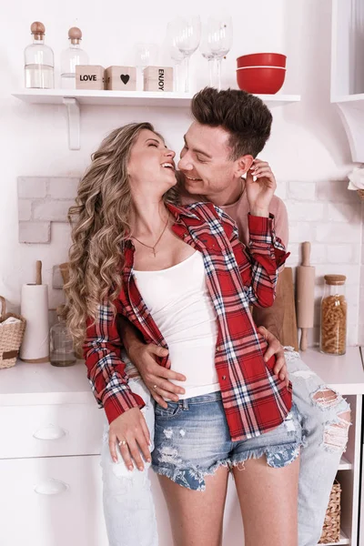 Lyckliga unga par i kärlek kramas och har roligt i köket på Alla hjärtans dag på morgonen. Snygg man och kvinna med långt hår är avkopplande hemma. — Stockfoto