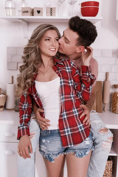 Ein glückliches junges verliebtes Paar umarmt sich und amüsiert sich am Valentinstag morgens in der Küche. stilvoller Mann küsst Frau in den Nacken und entspannt zu Hause. — Stockfoto