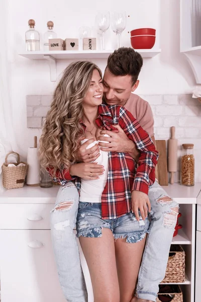 Feliz jovem casal apaixonado estão abraçando e se divertindo na cozinha no dia dos namorados na parte da manhã. Homem elegante segura as mãos sobre o peito da mulher e relaxante em casa . — Fotografia de Stock