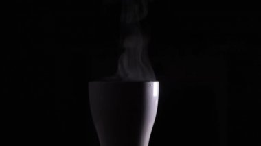 Steam from a white cup with boiling water. A trickle of steam rises from a cup of hot coffee. Absolutely black background, you can use to overlay an object. Steam over a cup of hot coffee or tea
