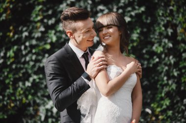 Amazing smiling wedding couple. Pretty bride and stylish groom. groom and bride posing in front wall with green ivy