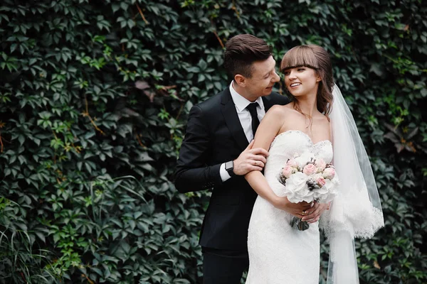 Sorridente coppia di nozze. Bella sposa e sposo elegante. sposo e sposa in posa nella parete anteriore con edera verde — Foto Stock