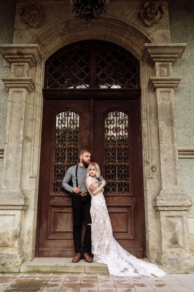 Stylish young man with beard and woman in luxury long dress on wedding day near the castle. Romantic love in vintage atmosphere street. — ストック写真