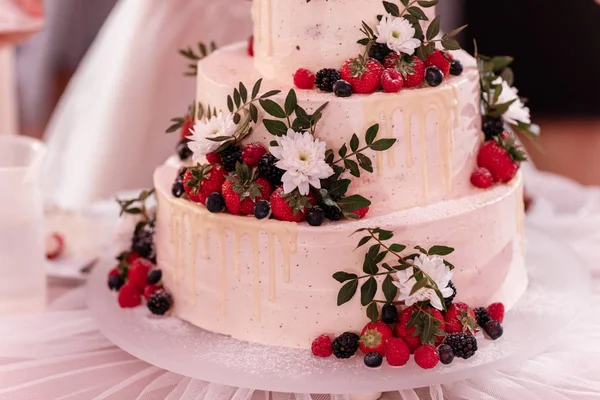 white cake decorated with berries and white flowers on a table at wedding party. wedding day.