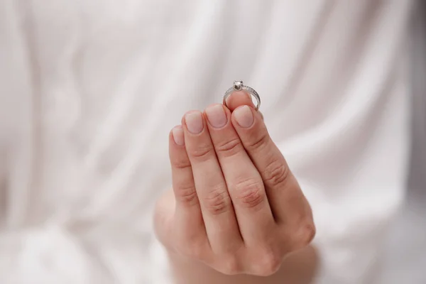 Mão feminina segurando anel de casamento feito de ouro branco e diamantes em um fundo branco. Luxo anel de proposta caro. Noiva no dia do casamento . — Fotografia de Stock