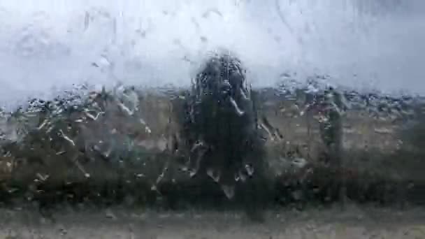 З вікна автомобіля видно дощ, що падає на скло, а розмитий фон це будівля, шторм або гроза. . — стокове відео
