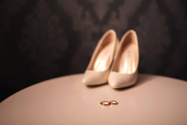 Dos anillos de oro de boda y zapatos femeninos de novia de la novia. compromiso. detalles de la decoración de la boda artículos novia y novio en la mesa blanca. mañana de la novia — Foto de Stock