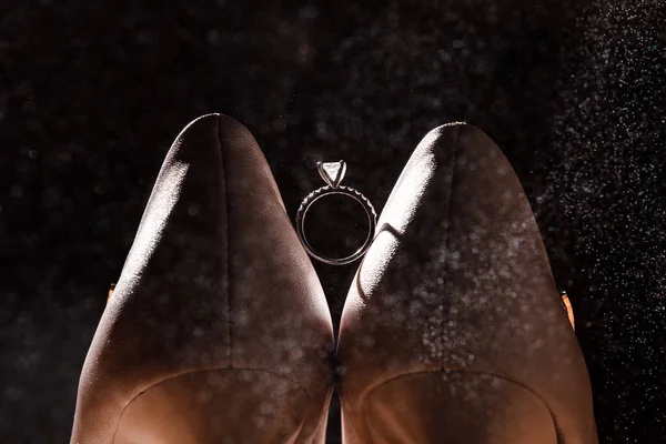 Anillo dorado con diamante entre par de zapatos blancos sobre fondo oscuro — Foto de Stock