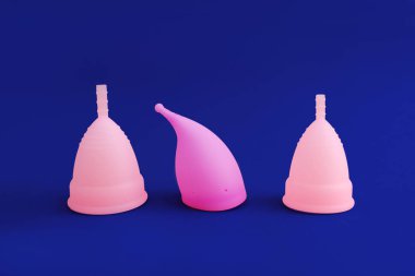 Mavi arka planda izole edilmiş üç farklı pembe silikon adet bardağı. Kadın hijyeni kavramı,