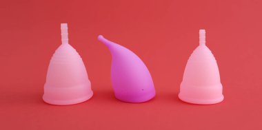 Kırmızı arka planda izole edilmiş üç farklı pembe silikon adet bardağı. Kadın hijyeni, jinekoloji, sağlık kavramı