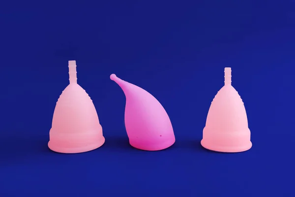 Три различных розовых многоразовые силиконовые менструальные чашки изолированы на синем фоне. Концепция женской гигиены , — стоковое фото