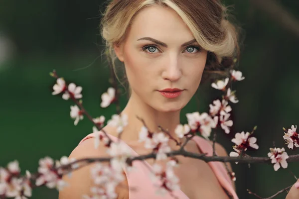 Portret van jonge mooie blonde vrouw in roze jurk in de buurt van bloeiende boom met witte bloemen op een zonnige dag. Lente, meisje bij een bloeiende boom — Stockfoto