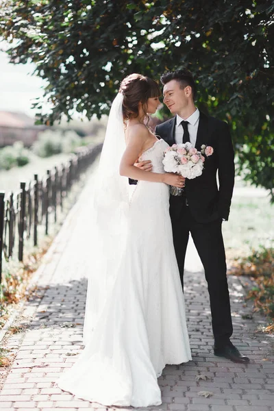 Весільна пара в парку. Наречена в стильній і красивій розкішній білій сукні, завісі і букет в руках. Наречений в чорному костюмі . — стокове фото