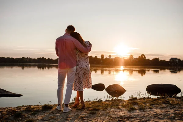 Pareja abrazándose al atardecer. Hermosa pareja joven en el amor caminando a lo largo del lago al atardecer en los rayos de luz brillante. enfoque selectivo. concepto de familia, confort, seguridad —  Fotos de Stock