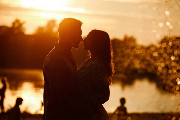 Silhouette eines verliebten Paares, das sich bei Sonnenuntergang am See umarmt. schönes junges verliebtes Paar, das bei Sonnenuntergang im hellen Licht am Ufer des Sees spaziert. Kopierraum. Selektiver Fokus — Stockfoto