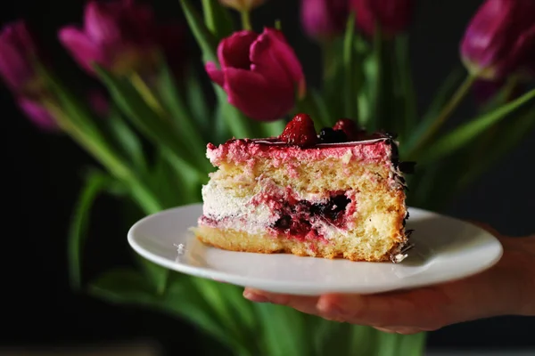 Rebanada Pastel Bayas Plato Blanco Cerca Hermosas Flores Tulipanes Mujer — Foto de Stock