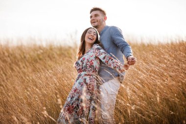 Güzel genç bir çift gün batımında çimlerle bir tarlada sarılıyor. Şık bir erkek ve kadın dışarıda eğleniyor. Aile kavramı. Boşluğu kopyala
