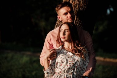 Birbirlerine aşık güzel bir çift yaz parkında sarılıp gülümsüyor. Pembe gömlekli şık bir adam ve elbiseli bir kadın birlikte eğleniyorlar. Aşk hikayesi. Boşluğu kopyala.