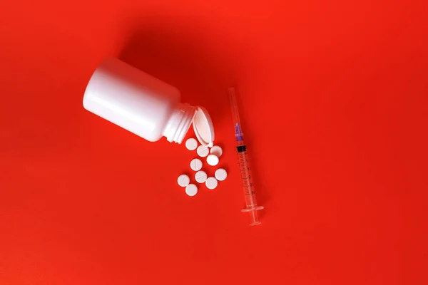 白色药丸分散在一个白色的罐子里 注射器在红色的背景上 有选择的重点 健康的概念 — 图库照片