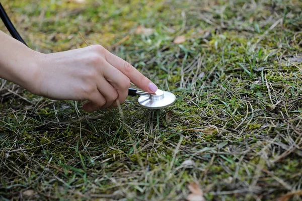 hand woman is listening to the ground with stethoscope in the park. concept love the environment. selective focus. copy space