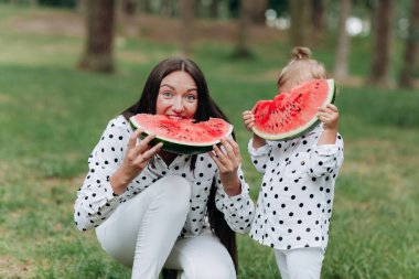 Mutlu anne ve kızı yaz parkında karpuz yiyorlar. Parkta karpuz yiyen mutlu bir aile. Anne ve kızı birlikte vakit geçiriyorlar. Diyet, vitaminler, sağlıklı gıda konsepti.