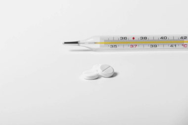Mavi arka planda bir sürü hap ve tablet var. İzole edilmiş. Uzayı kopyala Beyaz arka plan ve termometrede beyaz kapsüller. Soğuk algınlığı tedavisi.
