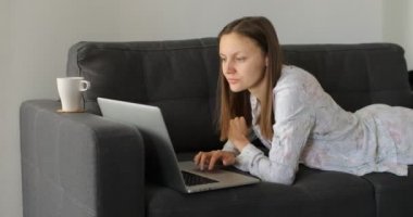 Ciddi genç kadın serbest çalışan, bilgisayarında e-posta yazan, bilgisayarını evdeki kanepede çalışmak için kullanan, uzaktaki internet işiyle meşgul bir kadın kullanıcı..