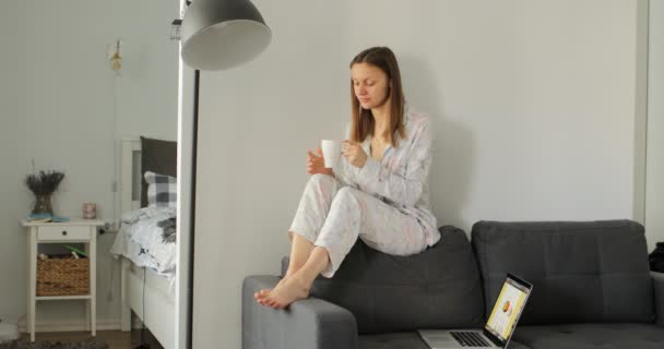 Dívka pije kávu nebo čaj na gauči. Žena pracuje, učí se a používá notebook v místnosti. Na volné noze. Psaní, psaní. Koncepce komunikace a technologie. — Stock video