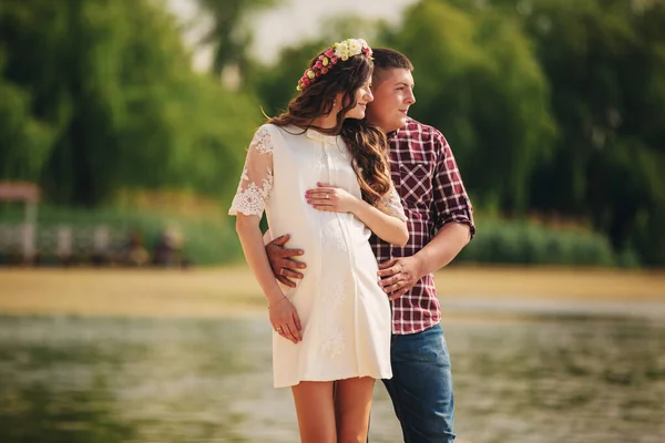 Young happy romantic pregnant couple hugging on nature near lake in summer park. Pregnant woman expecting a baby. Future mom and dad, family. mothers, fathers day — Stock Photo, Image