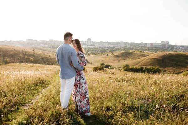 Mooi jong stel knuffelen in een veld met gras bij zonsondergang. stijlvolle man en vrouw die plezier hebben buiten. familieconcept. kopieerruimte. — Stockfoto