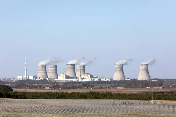 view of a nuclear power plant. View of smoking chimneys of nuclear power plant, power lines and forest, under blue sky with white clouds.