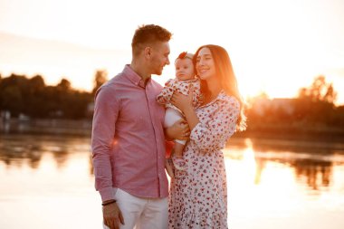 Baba, annem gün batımında göl kenarında kızını kucaklıyor. Yaz tatili kavramı. Anneler günü, babalar günü, bebekler günü. Aile doğada birlikte vakit geçiriyor. Aile görünüşü. seçici odak.