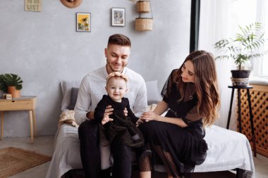 Güzel, genç bir aile şık bir yatak odasında yatakta oturuyor, anne, baba ve kız bebek evde. Anneler günü, babalar günü, bebekler günü. Aile birlikte vakit geçiriyor. Aile görünüşü. seçici odak.