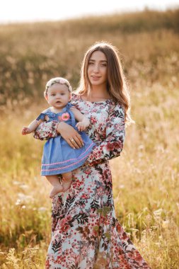 Güneşli bir günde, güzel anne ve küçük kızının açık havada çekilmiş bir portresi. Anneler günü, bebekler günü. Aile yaz tatili konsepti. seçici odak.